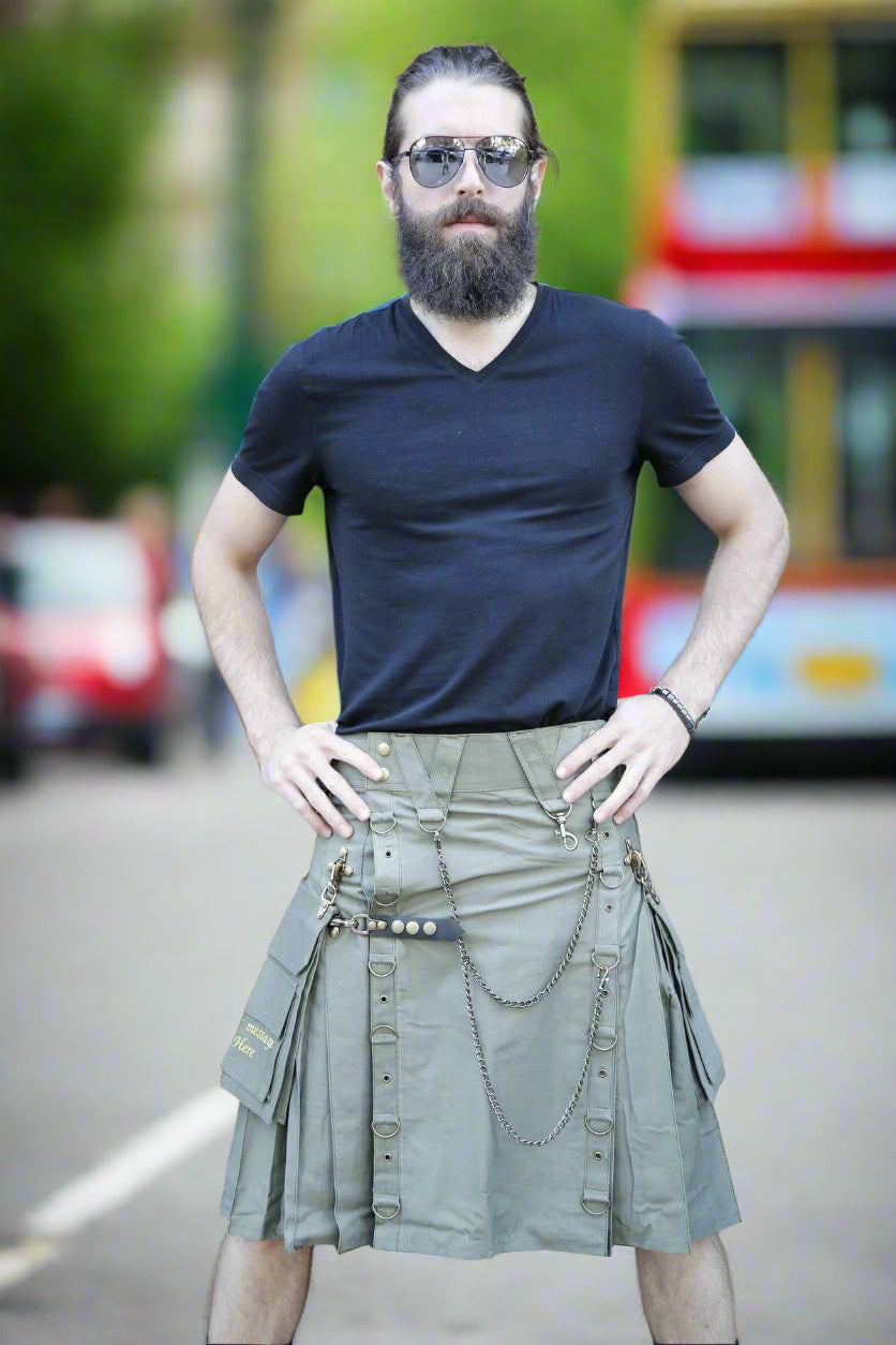 Man wearing a black t-shirt and green kilt standing in front of a glass door.